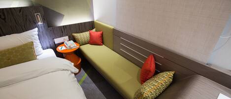 A hotel room with a bed, a sofa, a small table with a telephone, and a book on the table.