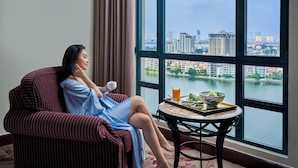 A person in a striped armchair by a window with a table and breakfast items. - Sheraton Hanoi Hotel (Hanoi)