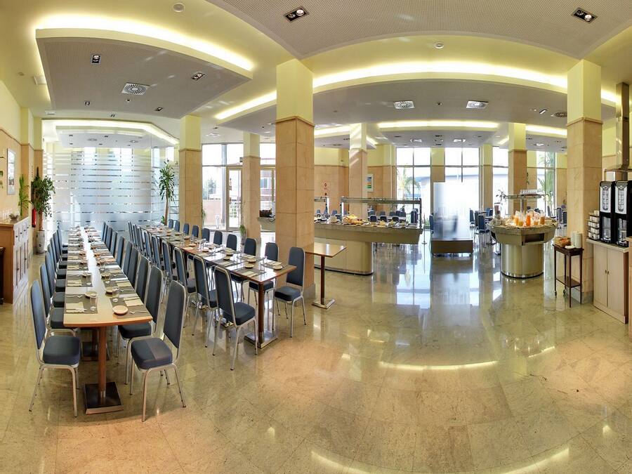 Un amplio comedor con mesas y sillas largas, una estación de buffet y una barra de café.