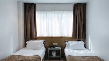 A hotel room with two beds, a nightstand, a window with curtains, and a light switch on the wall.