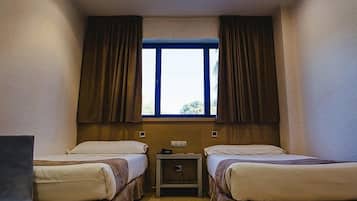 A small, well-lit room with two beds, a small table, and a window with curtains.
