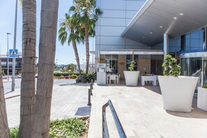 Un edificio moderno con fachada de vidrio, zona de estar exterior y palmeras.