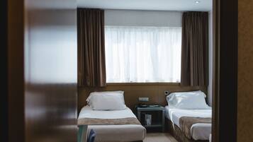 Ein Hotelzimmer mit zwei Betten, einem Nachttisch, einem Fenster mit Vorhängen und einer Wandleuchte.