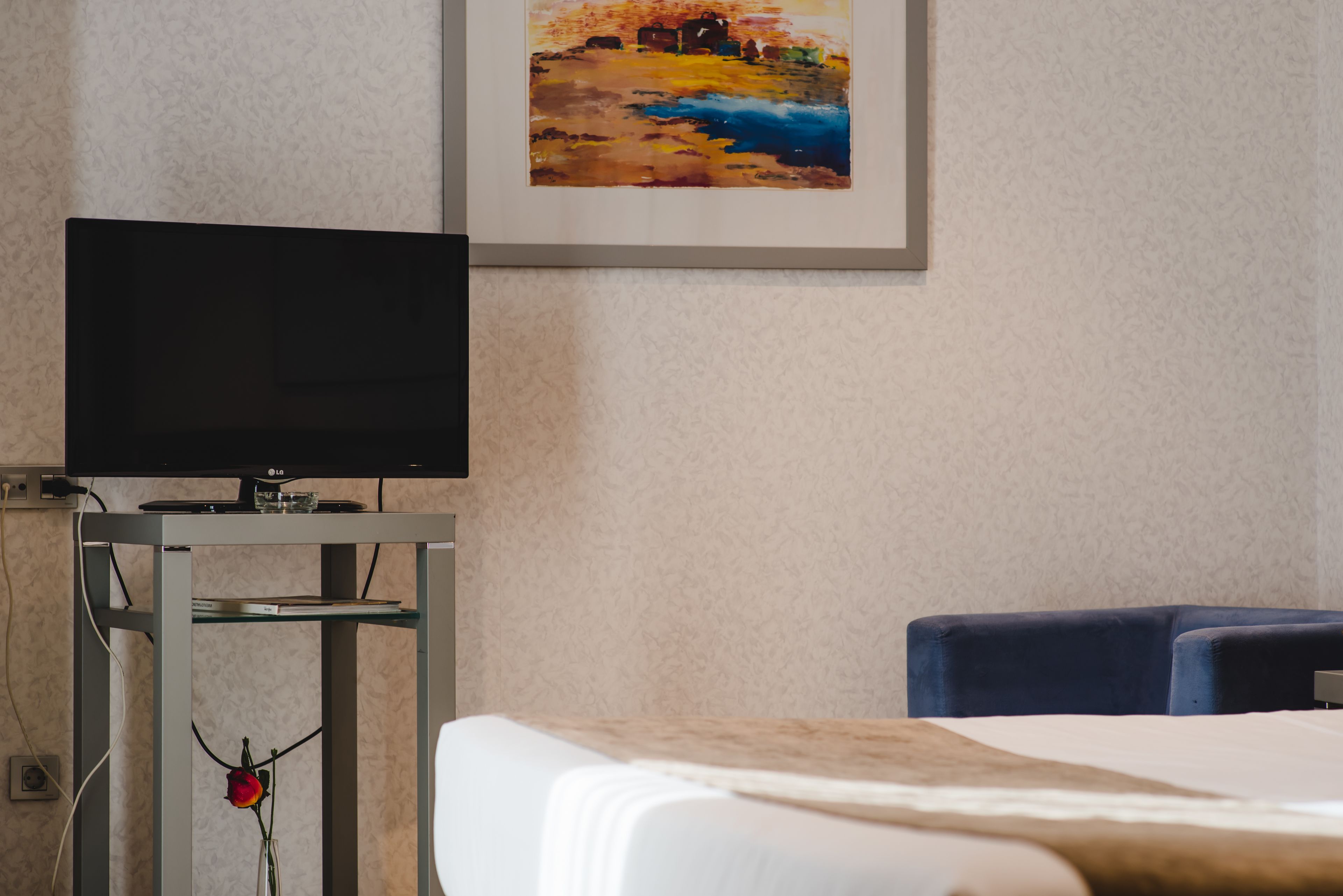 Una habitación de hotel con una cama, un televisor sobre un mueble, un cuadro en la pared y un escritorio con un jarrón de flores.