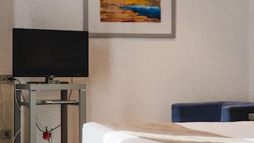 Una habitació d'hotel amb un llit, una televisió sobre un suport, un quadre a la paret i una taula amb un ram de flors.