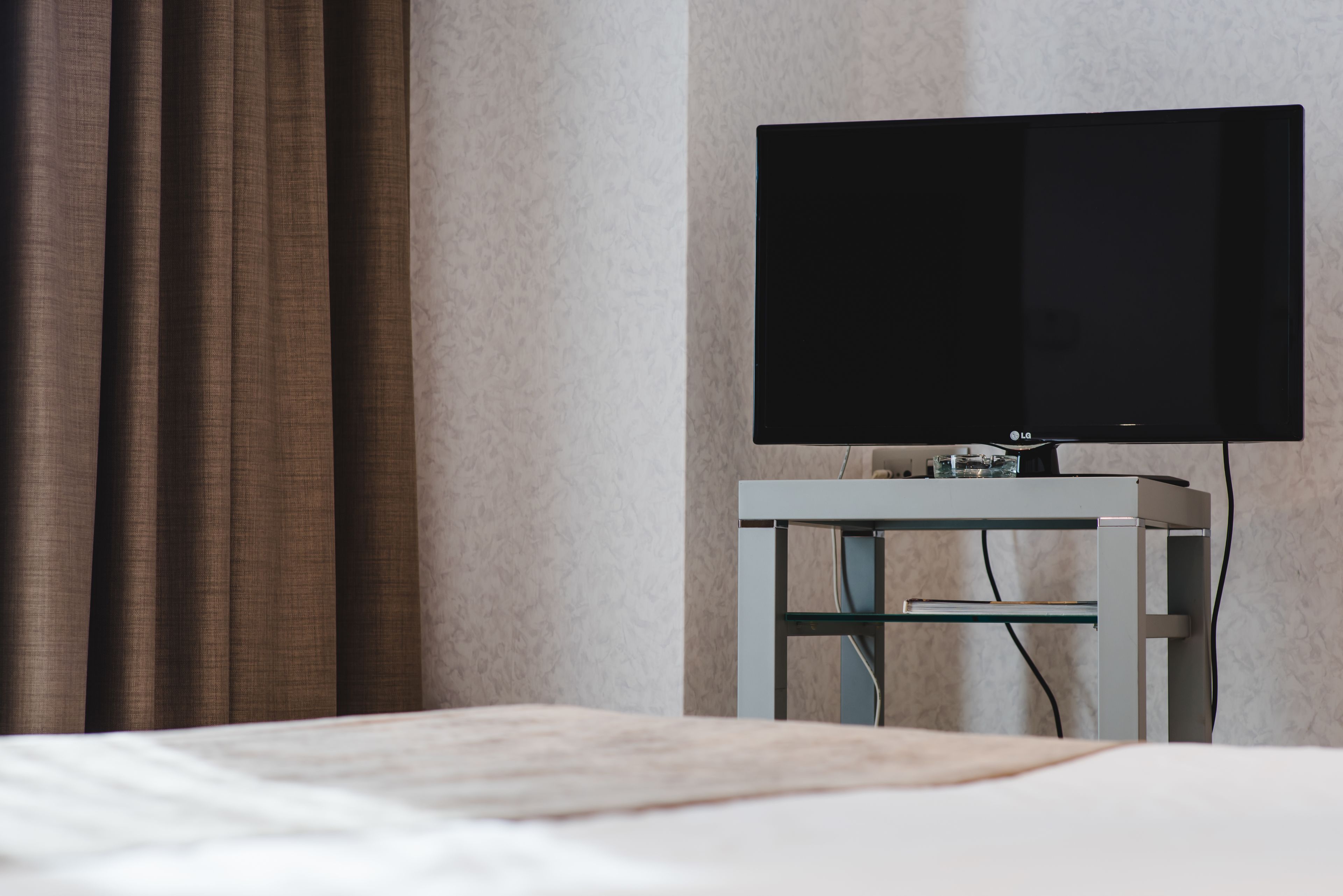 Una habitación de hotel con una cama, un televisor de pantalla plana sobre un mueble bajo y una cortina.