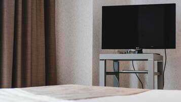Una habitación de hotel con una cama, un televisor de pantalla plana sobre un mueble bajo y una cortina.