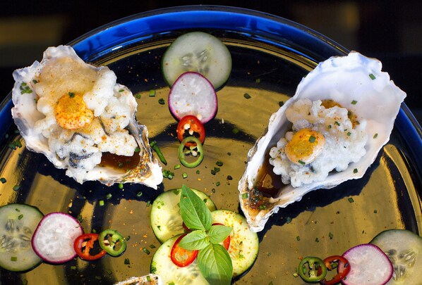 A seafood dish with oysters, cucumber slices, radish slices, and chili peppers on a blue plate. - Porto Zante Villas And Spa (Zakynthos)