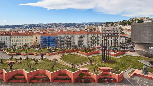 A cityscape with a park area featuring red planters and a statue, surrounded by buildings with red roofs and a distant view of hills. - Hotel Campanile Nice Centre - Acropolis (Nice)