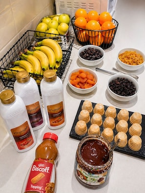 Una encimera de cocina con diversos alimentos, como plátanos, naranjas, frutas secas y frascos de condimentos.