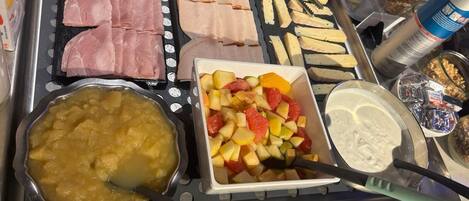 A buffet with various food items including meats, fruits, and a bowl of soup.