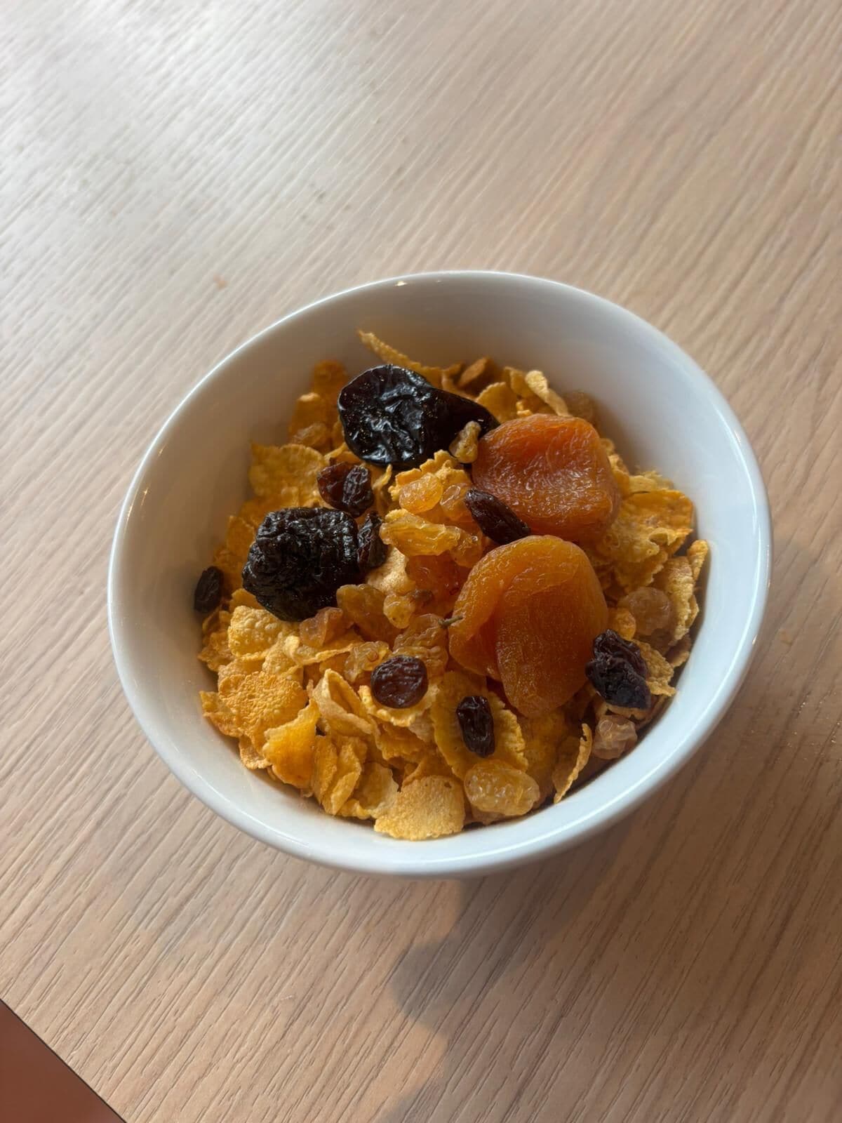 Een kom ontbijtgranen met rozijnen en gedroogd fruit op een houten ondergrond.