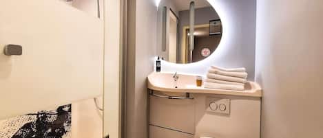 A modern bathroom with a glass-enclosed shower, a vanity with a sink and mirror, a toilet, and a trash bin.