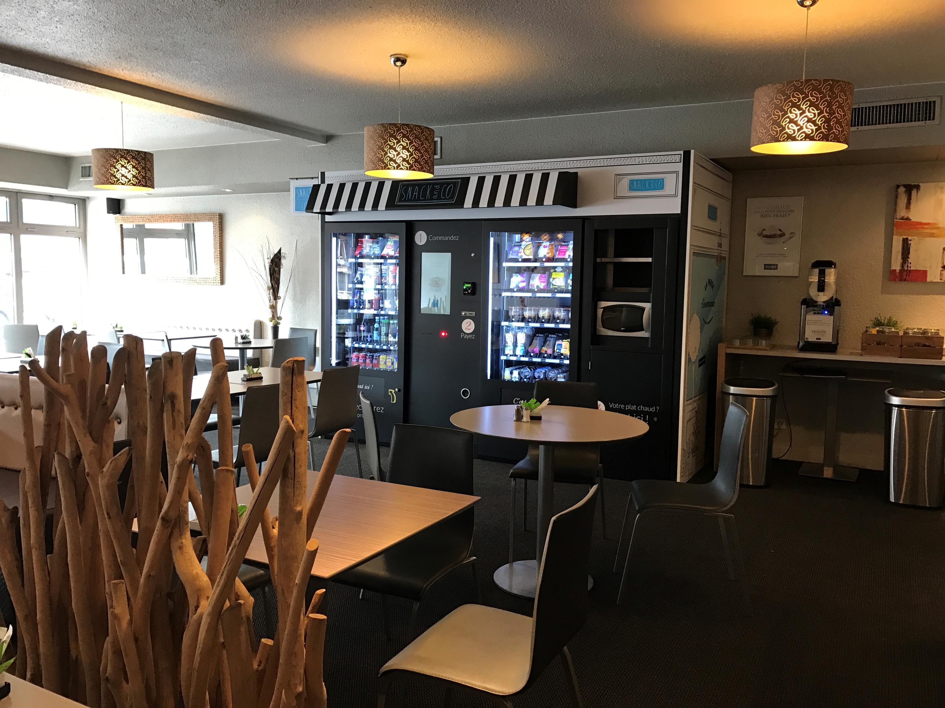 Un café moderne doté d’un bar, de tables et de distributeurs automatiques.