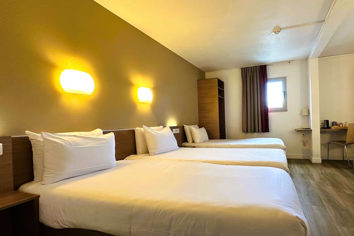 A hotel room with two beds, a desk, and a window with curtains.