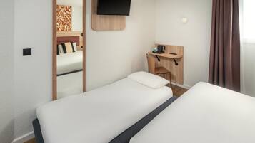 Une chambre d’hôtel avec deux lits simples, un bureau avec une chaise, un téléviseur fixé au mur et un petit coin salon avec une table et des chaises.