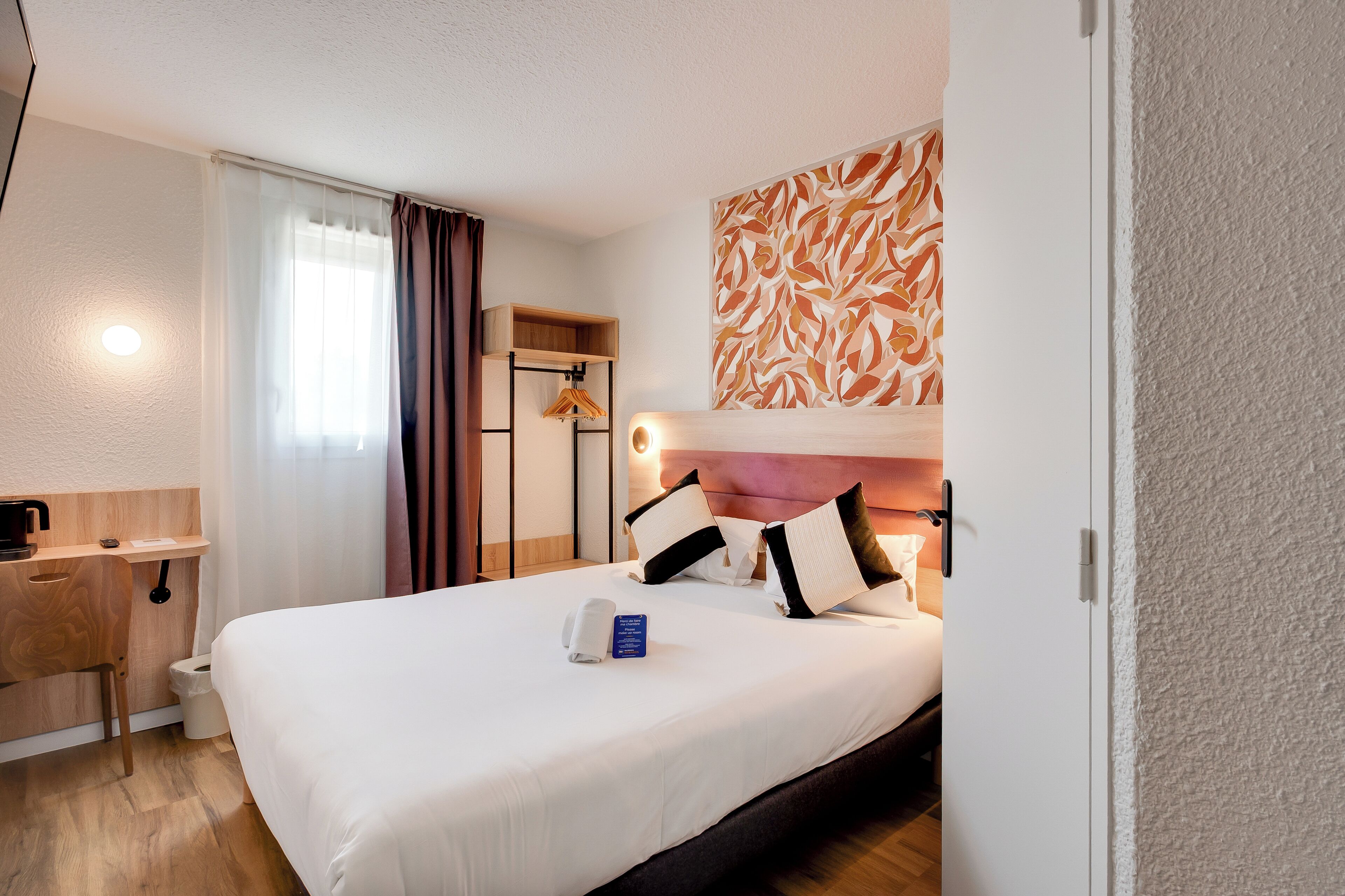 A hotel room with a bed, a bedside table, a small desk, a shower area, and a wall art piece.