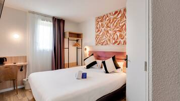 Een hotelkamer met een bed, nachtkastje, een klein bureau, een douchegedeelte en een kunstwerk aan de muur.