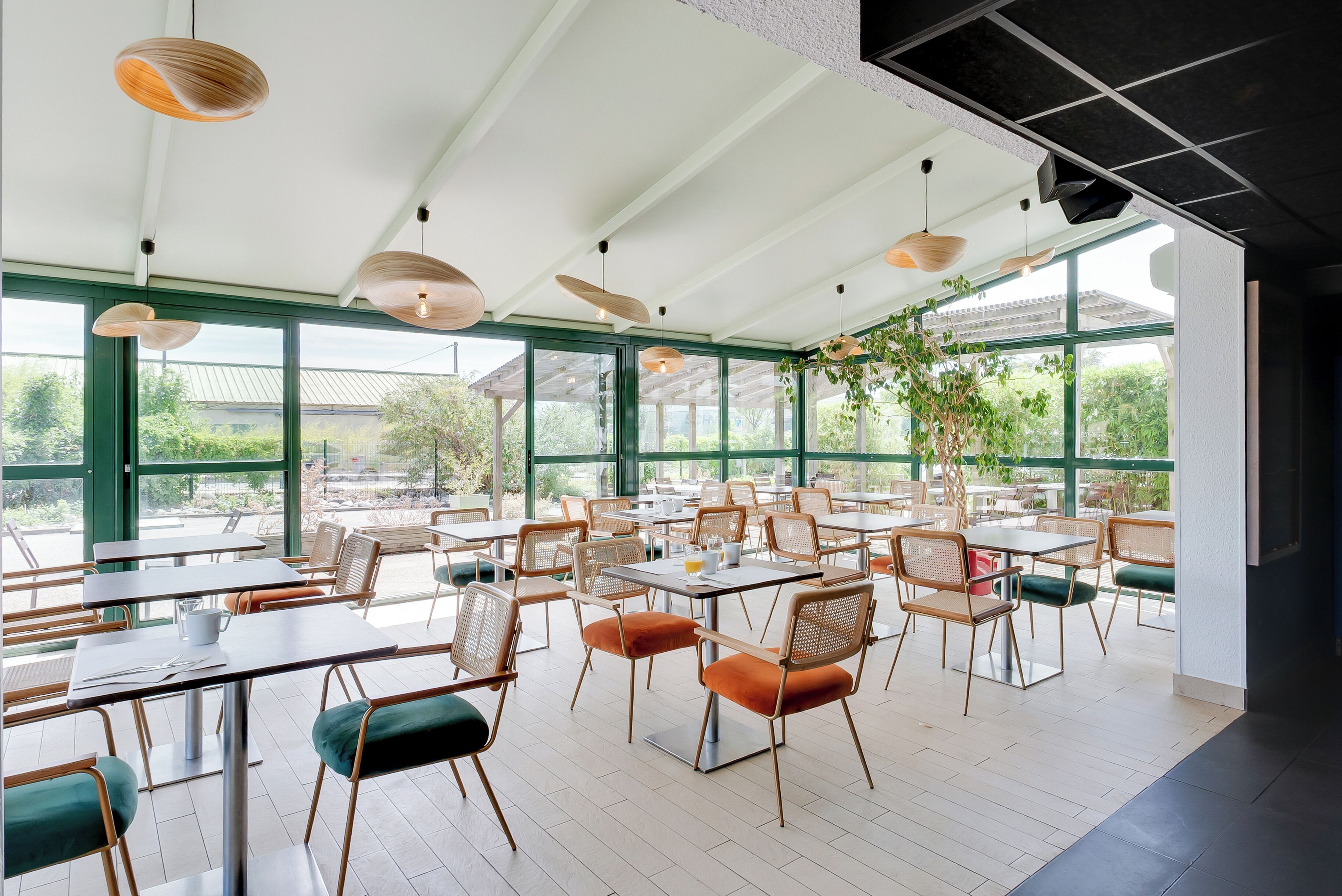Un'ampia sala da pranzo interna con tavoli e sedie, grandi finestre e lampadari a sospensione.