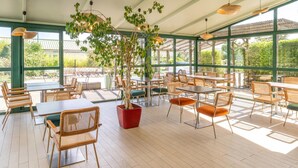 Un área de comedor al aire libre con sillas y mesas de mimbre, ventanas amplias y una planta en maceta.