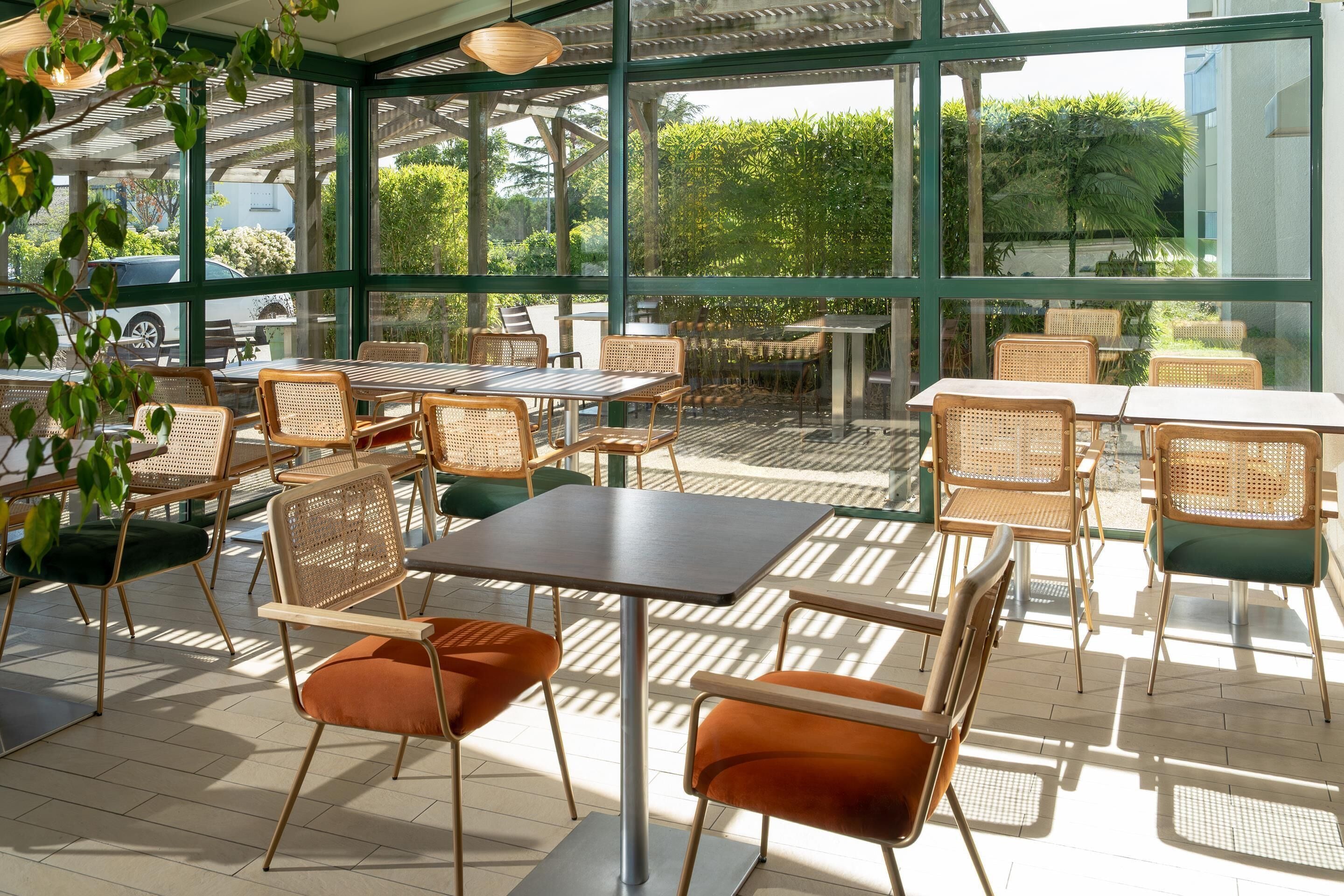 Un café al aire libre con mobiliario de mimbre y paredes de vidrio.