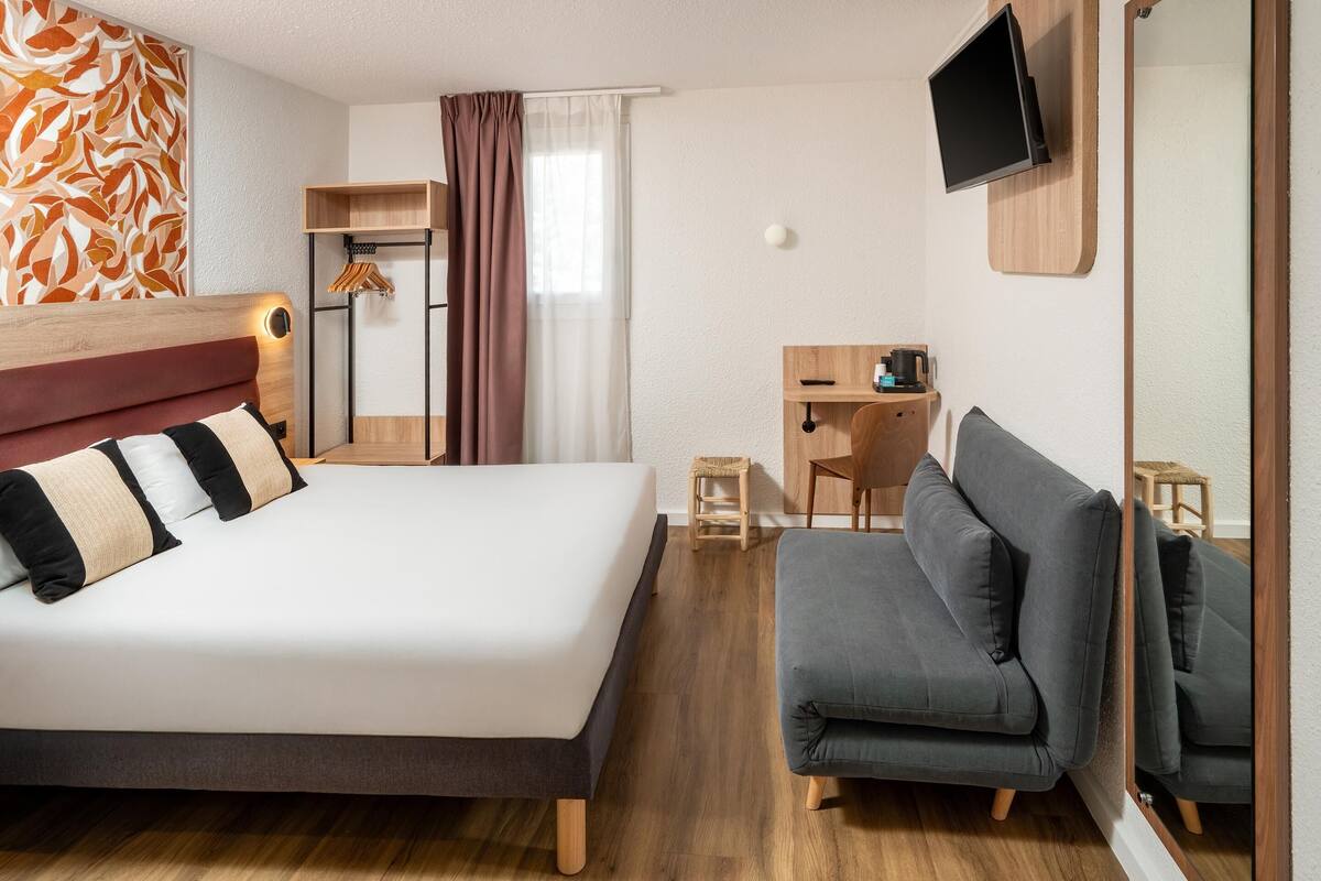 Ett modernt hotellrum med en stor säng, en soffa, ett skrivbord och en tv som är monterad på väggen.
