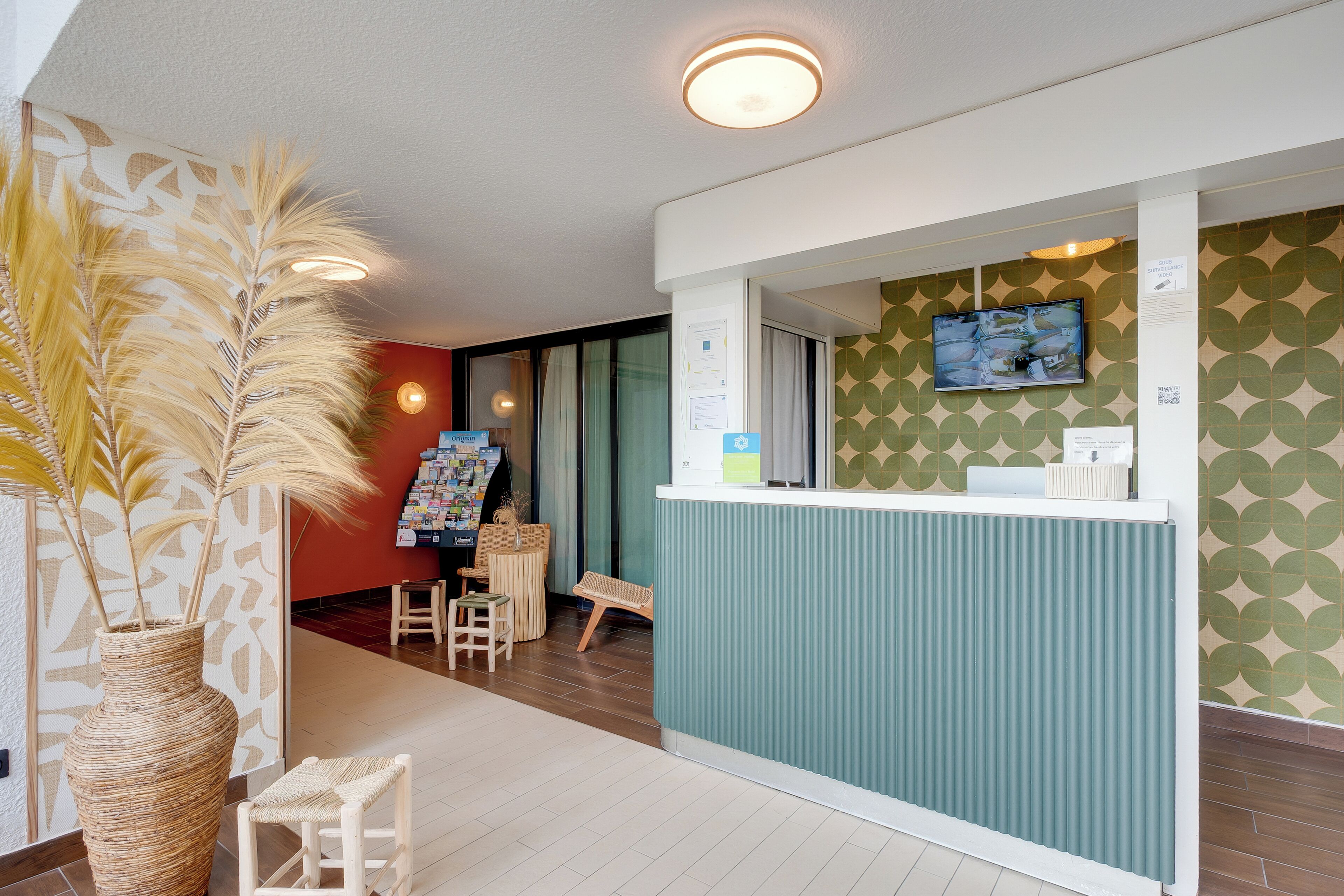 A reception area with a counter, a television mounted on the wall, a seating area with a chair and a small table, and a decorative plant.