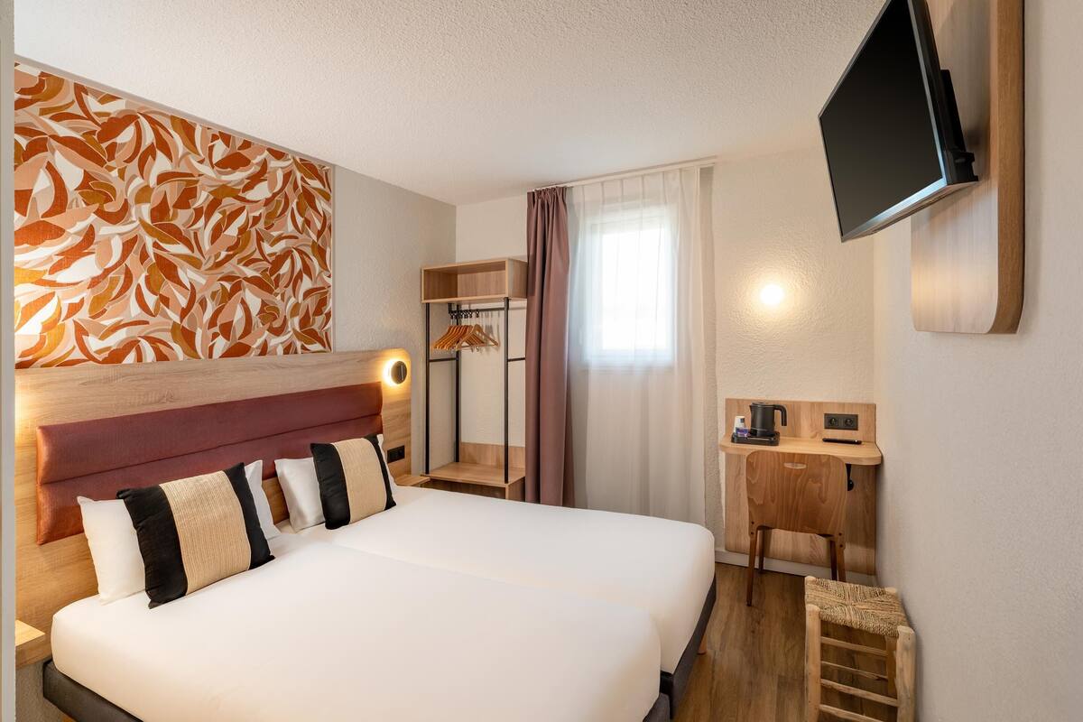 Ett hotellrum med en stor säng, ett skrivbord med en dator, en tv som är monterad på väggen och en sänggavel i trä.