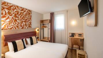 Habitación de hotel con una cama grande, un escritorio con computadora, un televisor montado en la pared y un cabecero de madera.