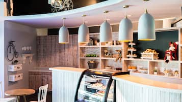 Um café moderno com balcão, vitrine de doces e luminárias pendentes.