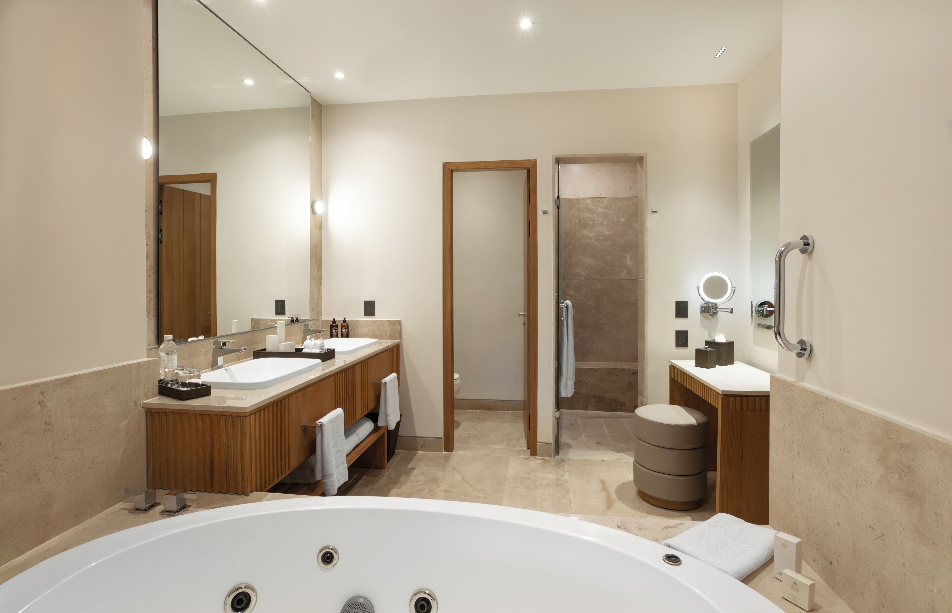 Ein modernes Badezimmer mit einer großzügigen Badewanne, zwei Waschbecken, einer Duschkabine und einem Waschtisch mit Spiegel.