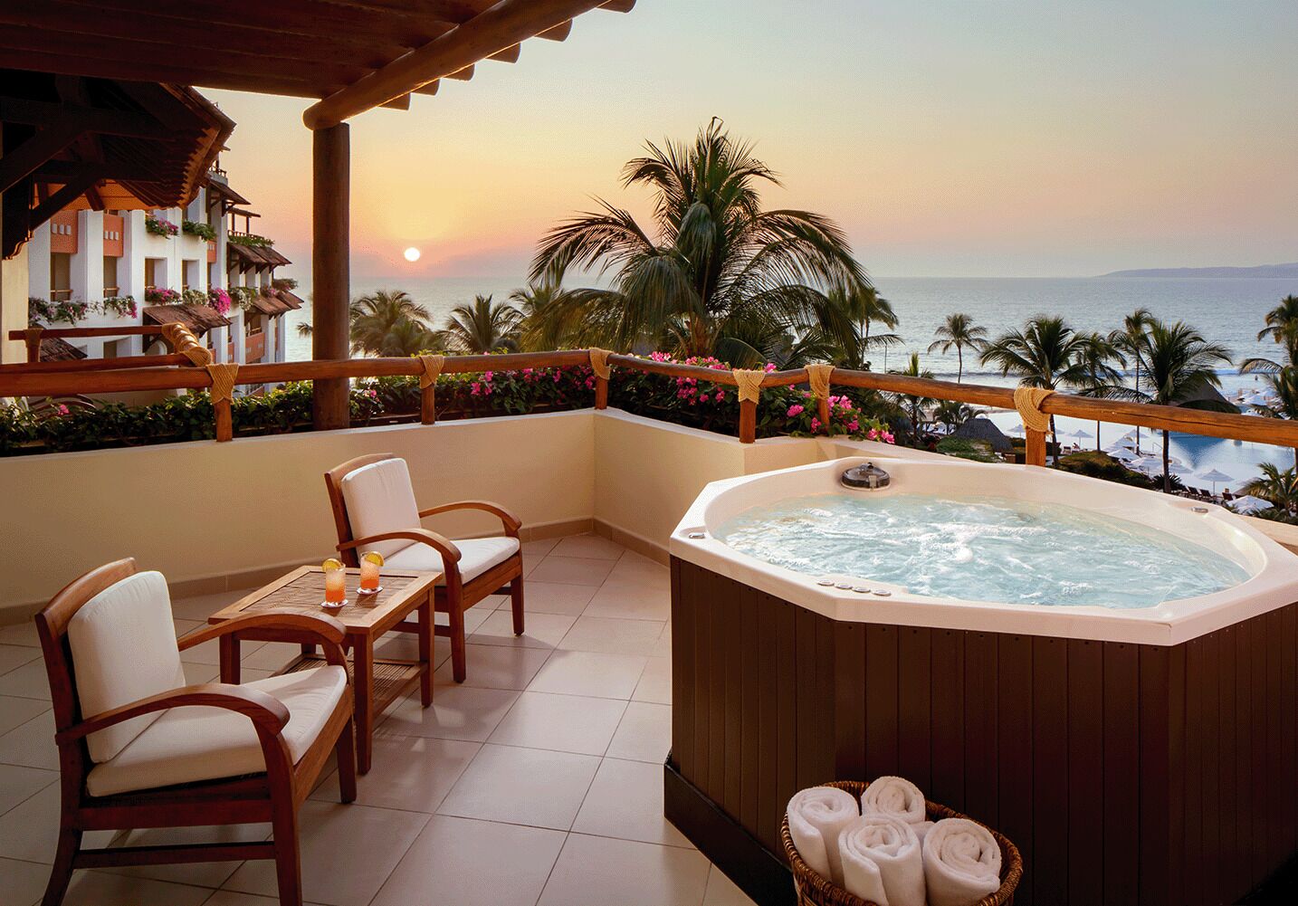 A balcony with a hot tub, chairs, and a table with drinks.