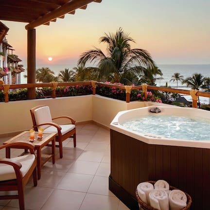A balcony with a hot tub, chairs, and a table with drinks.