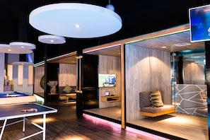 A modern lounge area with a pool table, seating, and a large screen.