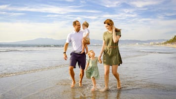 Una familia caminando en la playa, con cielo despejado y montañas al fondo.
