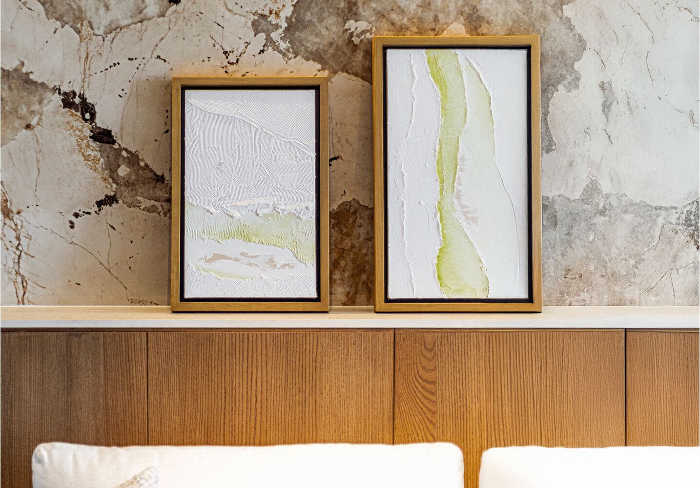 Two framed abstract paintings on a wooden cabinet against a textured wall.