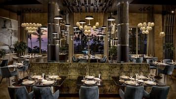 Un restaurante con una zona de asientos central, varias mesas de comedor y vistas al atardecer a través de amplias ventanas.