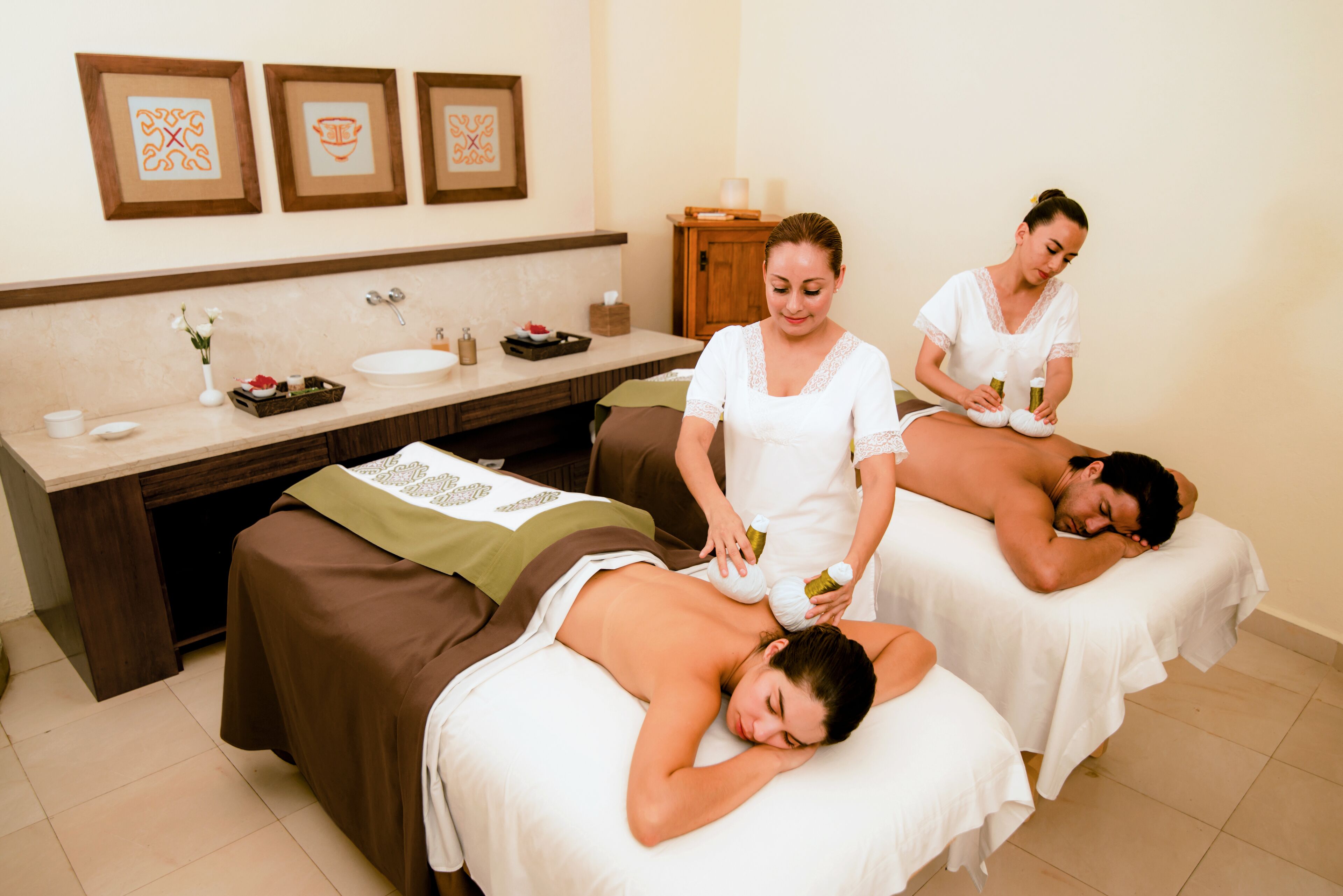 Une salle de spa équipée de deux tables de massage, d’un bureau en bois avec un lavabo et de tableaux encadrés accrochés au mur.