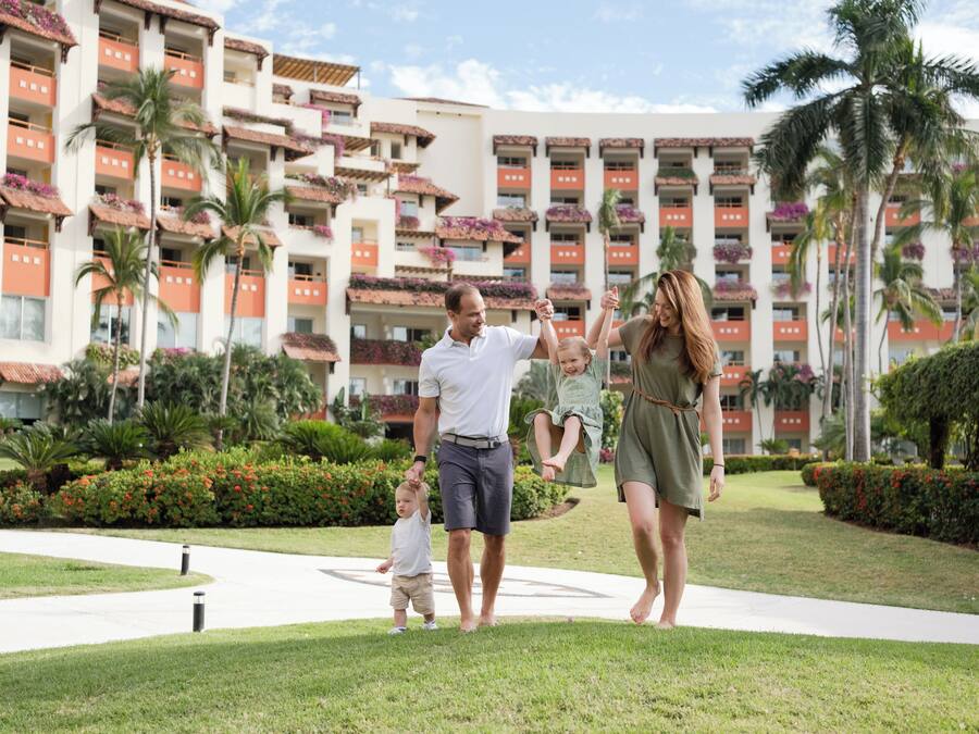 A family walking on a pathway in front of a hotel with multiple balconies and palm trees.