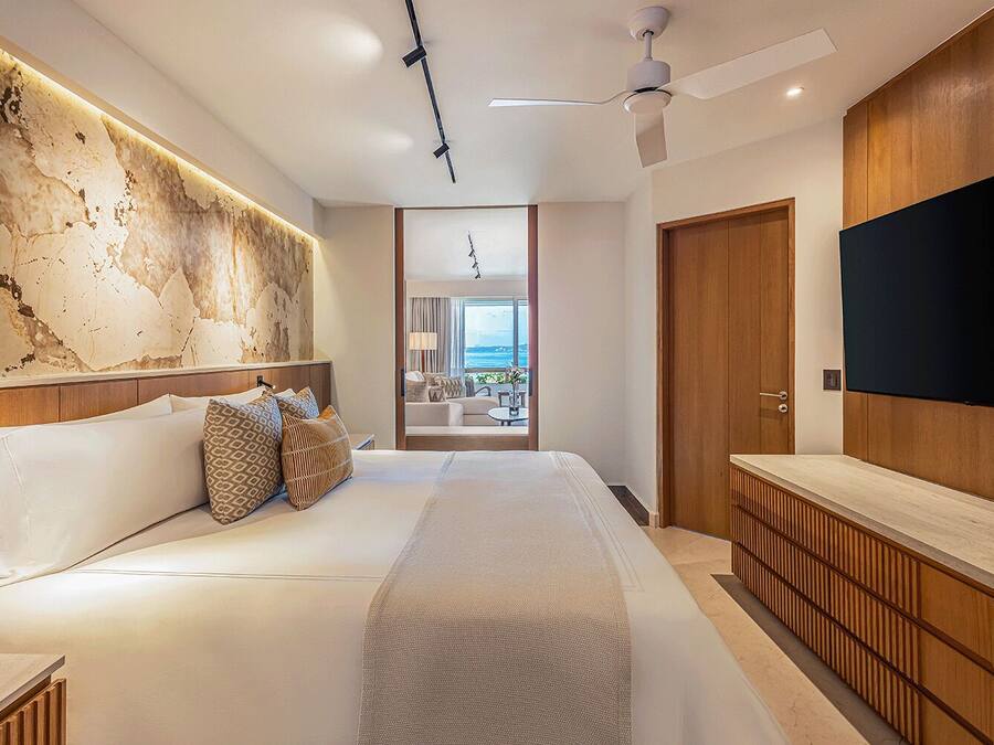 A modern hotel room with a large bed, a wooden headboard, a flat-screen TV, and a view of the outdoors.