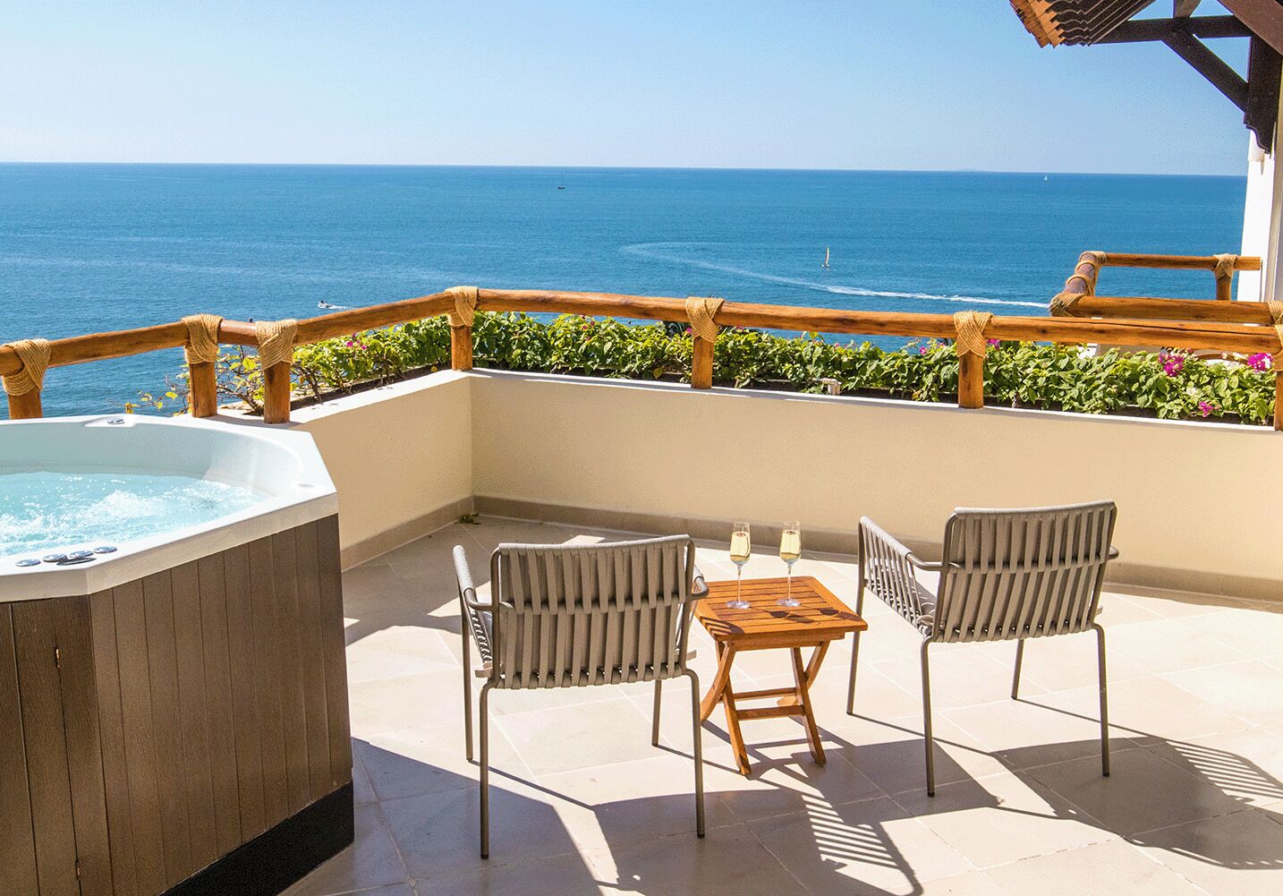 A balcony with a hot tub, two chairs, and a table with two glasses of champagne.