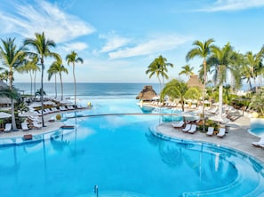 A large, clear blue infinity pool with lounge chairs and palm trees, overlooking the ocean. - Grand Velas Riviera Nayarit - All Inclusive (Nuevo Nayarit)