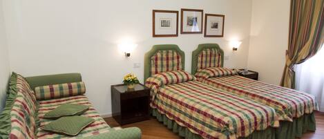 Una habitación con dos camas, un sofá y una mesita de noche con un jarrón de flores.