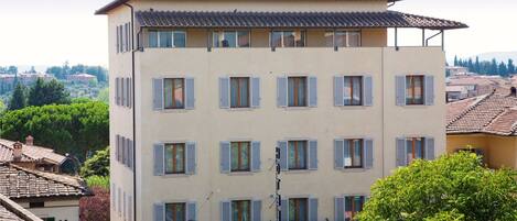 Un edificio de varios pisos con fachada plana, múltiples ventanas con persianas y un balcón con plantas.