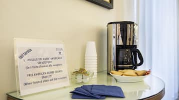 A coffee station with a sign offering free American coffee, a coffee maker, and a plate of cookies.