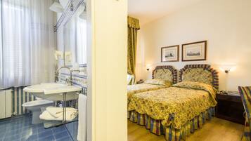 A bathroom with a sink, toilet, and shower, and a bedroom with two beds and a nightstand.