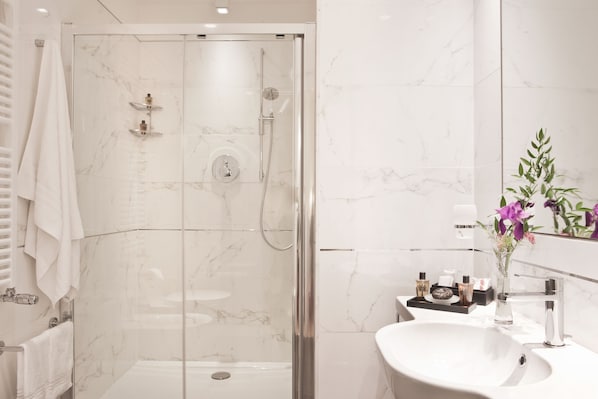 A modern bathroom with a glass-enclosed shower, a white sink, and a mirror with a vase of flowers.