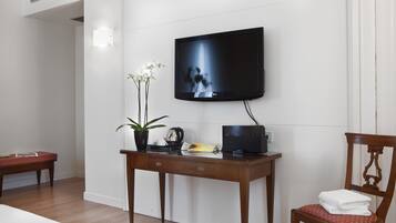Habitación de hotel con un escritorio de madera, un televisor montado en la pared, una silla con cojín rojo y una mesita con una planta y una tetera.