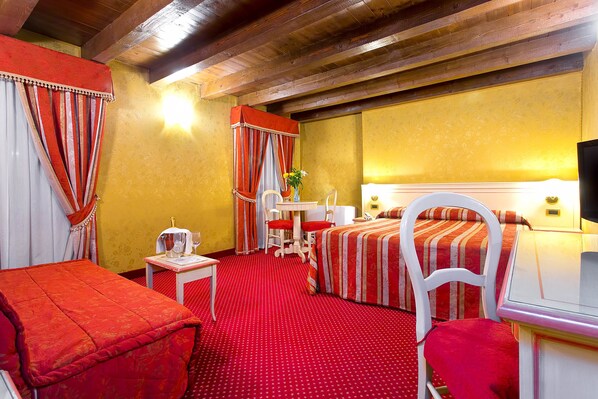 A hotel room with two beds, a desk, a chair, a small table with a lamp, and a window with curtains. - Ca' San Polo (Venice)