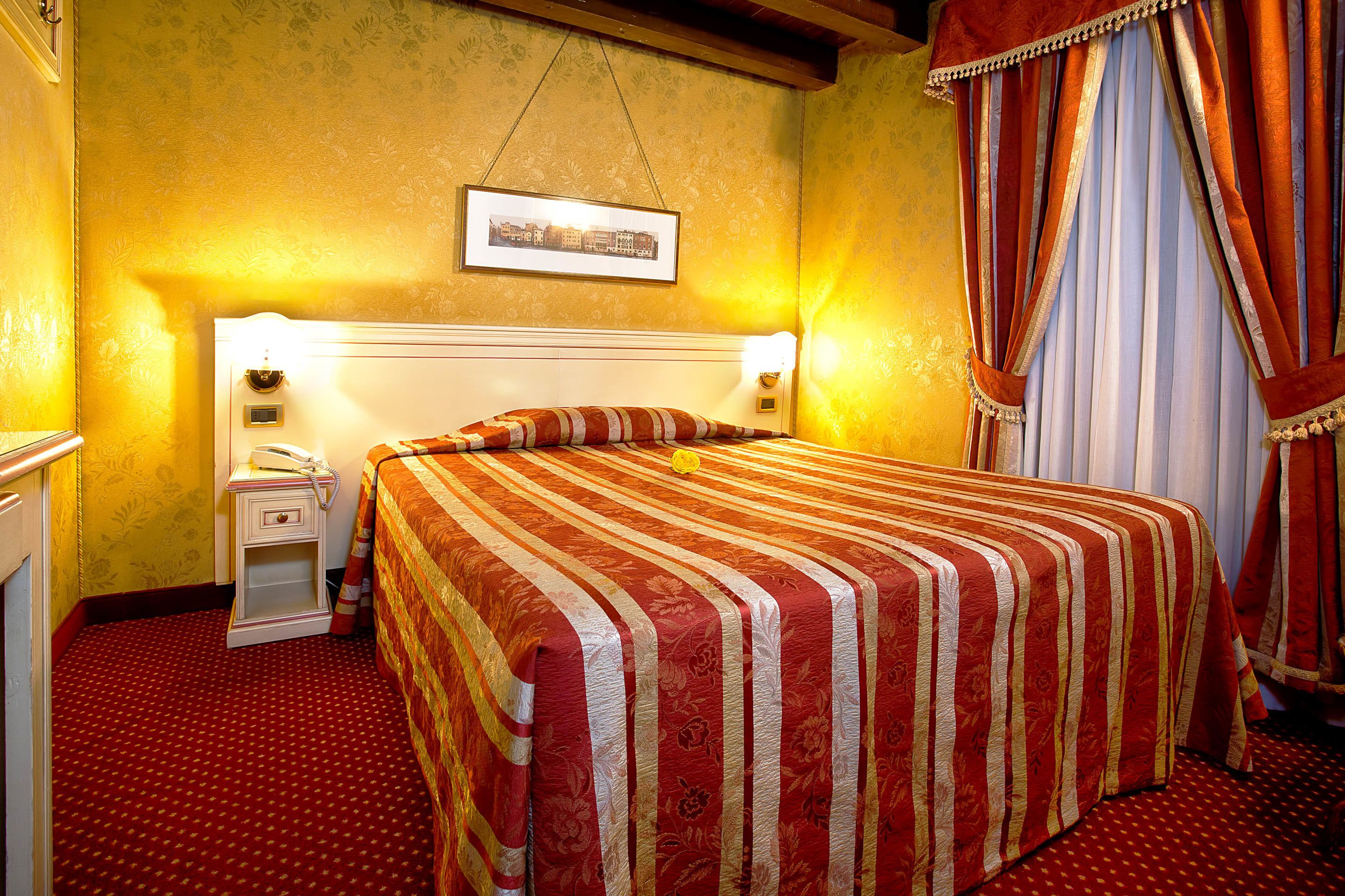 A hotel room with a large bed, a nightstand, a lamp, and a framed picture on the wall.